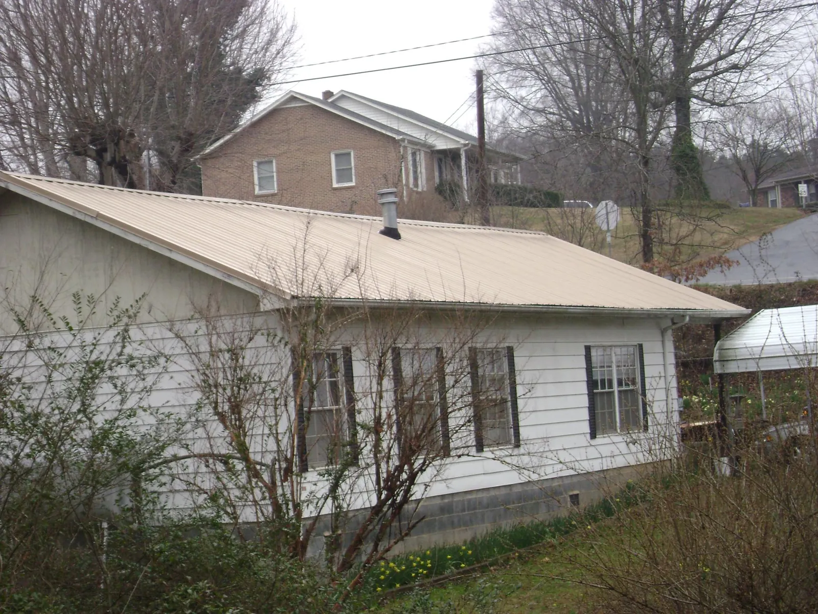 Tan metal roof on a white sided house set into a hillside — Commercial Roofing by Roofing Brothers in Silverstreet