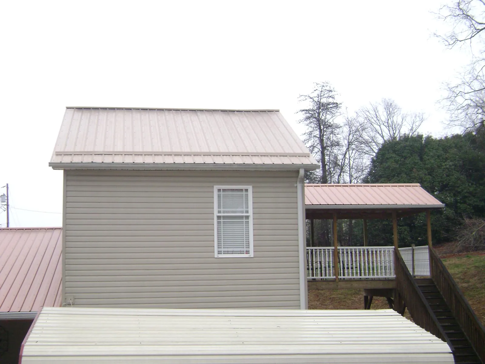 Tan metal roofs on a two story addition and attached porch, from a Roof Replacement job in Silverstreet